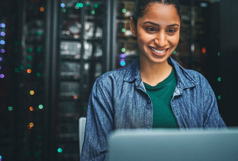 smiling woman in a server room using a laptop computer