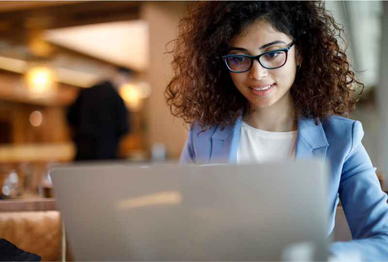 A woman smiling and looking at a laptop screen in front of her.