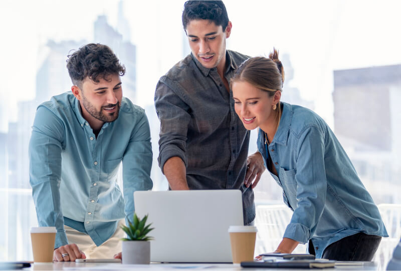 Two men and one woman looking at a laptop monitor on a desk in front of them all.