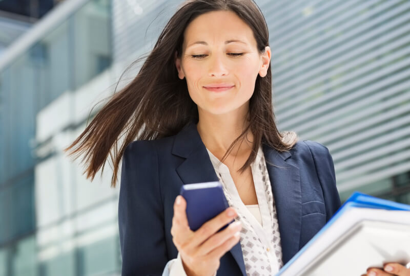 A woman smiling and looking at a smartphone held in her hand