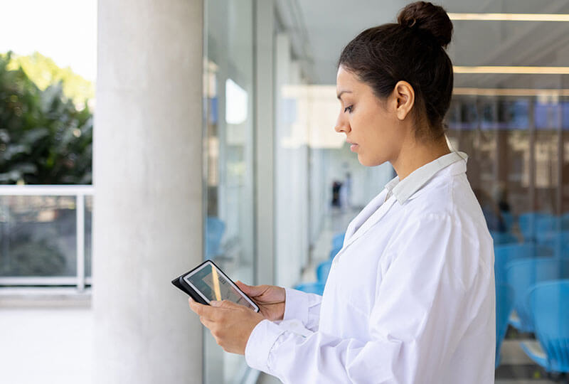 A woman in a lab coat interacting with a tablet device..